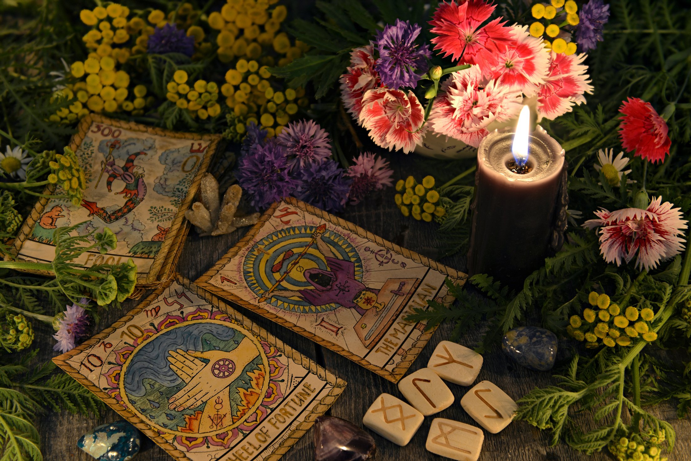 Still life with old tarot cards, black candle, runes, healing herbs and flowers